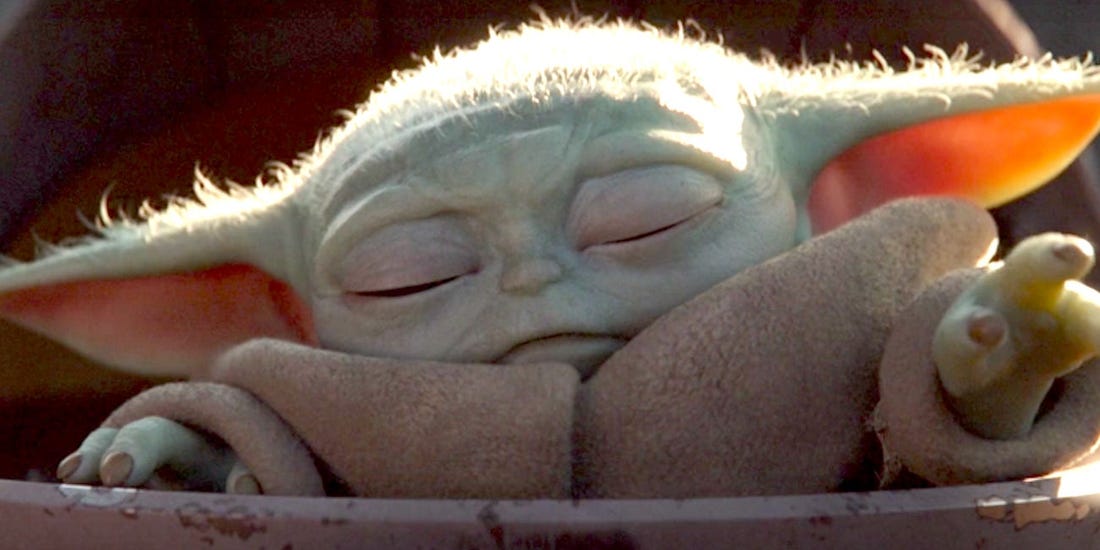 Baby Yoda, with eyes closed, reaches out with his left hand as if to use the Force.