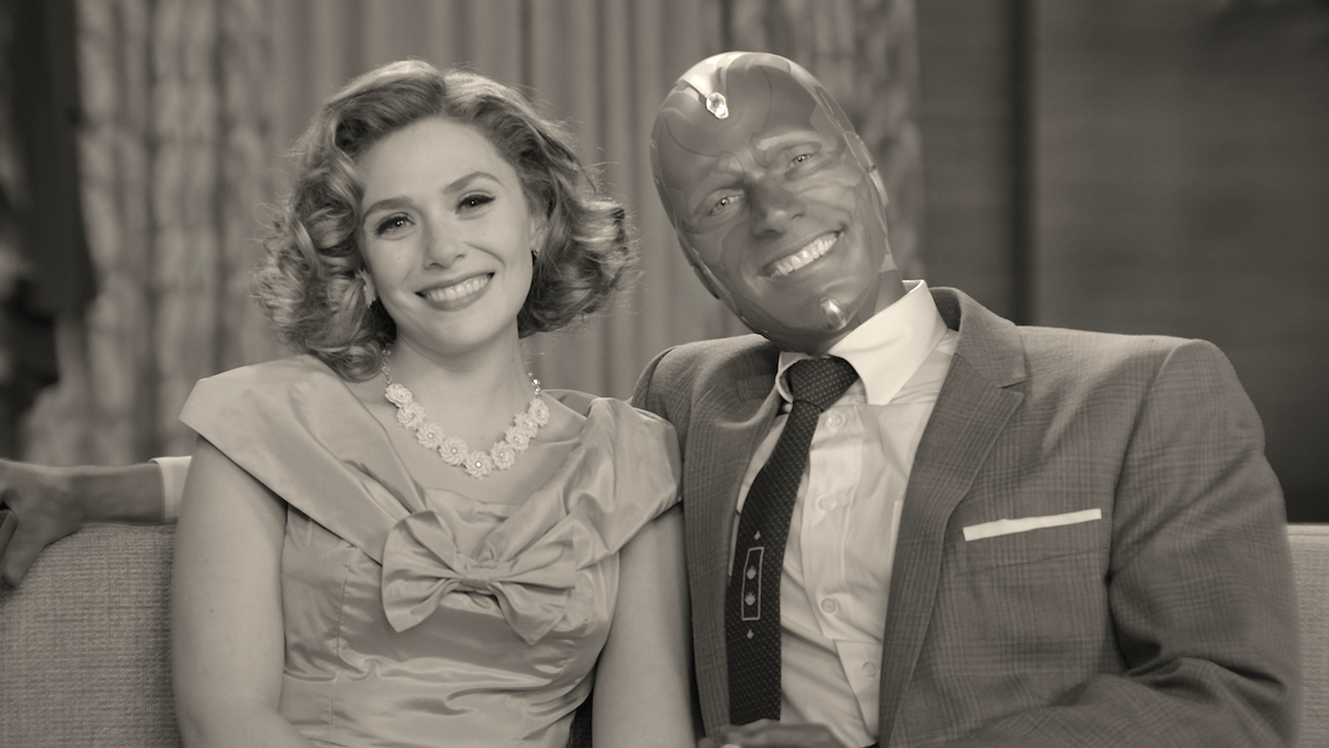 Elizabeth Olsen (as Wanda Maximoff) and Paul Bettany (as Vision) sit together, smile, and pose for the camera. The photograph is in black and white, to mimic the style of 1950s sitcoms.