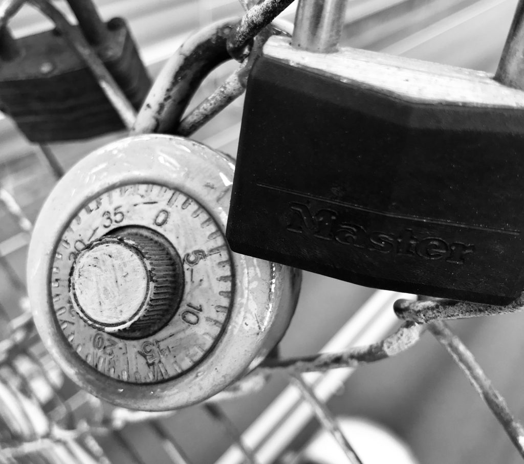 Black and white photo of 3 locks on a chain link fence